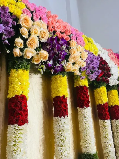 A close-up of a colorful floral garland used for stage or entrance decoration. I use a variety of fresh flowers like roses, chrysanthemums, and jasmine to create these thick, vibrant arrangements.