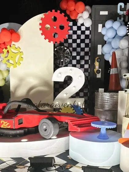 A dynamic shot of the stage, featuring a red Formula 1 car prop, a light-up number "2," and colorful gear accents for a "Two Fast, Two Curious" birthday.