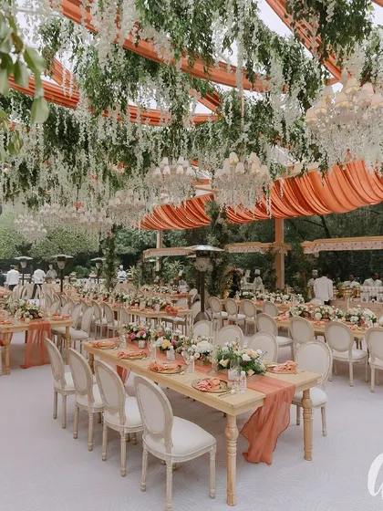 For this reception, we created a ceiling of hanging white wisteria and greenery over long dining tables. The peach-colored table runners add a soft pop of color to the otherwise neutral palette.