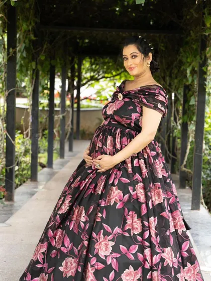 This black floral print gown is a unique and stylish choice for an outdoor maternity shoot, blending perfectly with the garden setting.