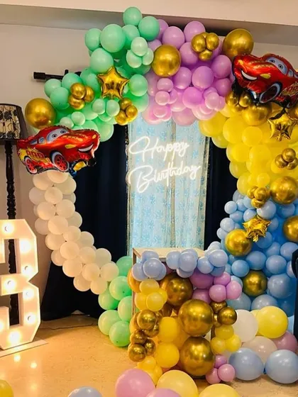 A colorful "Cars" themed birthday party for a 3-year-old. The decoration includes a full balloon ring with Lightning McQueen foil balloons and a light-up number "3".
