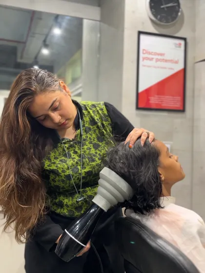 A student practices blow-drying curly hair using a diffuser. This specialized technique is crucial for defining curls and preventing frizz, and our students get hands-on practice to perfect it.