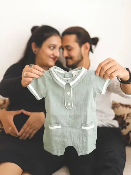 A sweet and creative baby announcement. The couple holds up a tiny baby romper, their faces close together, sharing a private, happy moment.