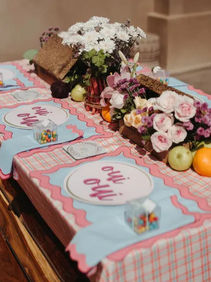 A close-up of the table setting from the Parisian Mehendi, featuring custom 'Oui Oui' plates, gingham-patterned linens, and fresh fruits, capturing the essence of a French cafe.