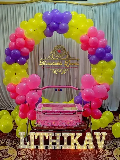 A colorful cradle ceremony decoration with a bright balloon ring framing the baby's cradle.