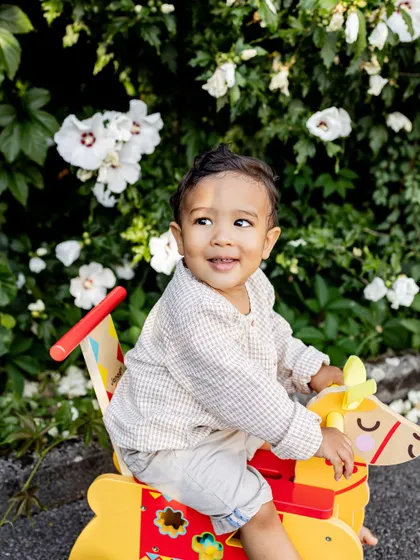 A happy toddler enjoying a ride on a rocking horse in the garden. Outdoor sessions are great for capturing active and playful children.