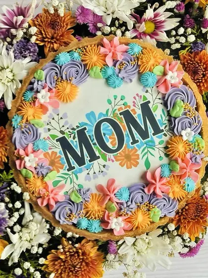 A top-down view of my Mother's Day special Chocolate Tart Hamper. The tart features an edible "MOM" design surrounded by colorful buttercream flowers, all framed by a real floral bouquet.