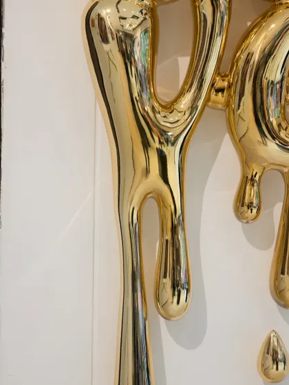 A detail of the dripping golden forms in the "Love Drip" sculpture, their fluid shapes conveying a sense of abundant emotion.