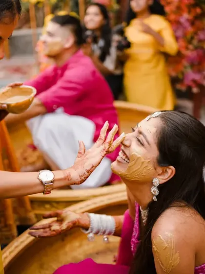 The bride's joyful smile as her sister or friend applies haldi. The shared laughter between them makes this a heartwarming and candid moment.