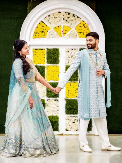 A happy, bright shot of a couple in pastel outfits, holding hands in front of a floral photo booth.