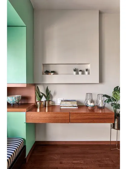 This study corner combines a rich wood desk with a refreshing mint green accent wall. A built-in niche provides a clean, recessed space for displaying small plants and decor, adding a personal touch to the workspace.