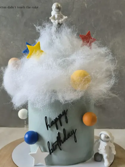 An out-of-this-world space-themed cake with an astronaut, planets, and stars, using cotton candy for a fluffy cloud effect.