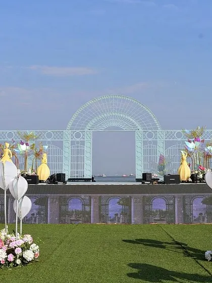 The full daytime setup of the varmala stage, with a modern aisle and a grand arched backdrop framing the Mumbai sea.
