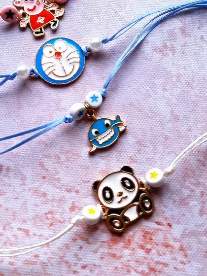 More character fun. This image shows a cute panda and a happy whale charm, perfect for kids who love animals. The Doraemon and Peppa Pig Rakhis are also part of this collection.