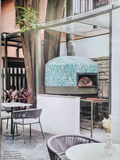 As featured in a magazine, this shot shows the beautiful mosaic-tiled pizza oven at Kana Cafe, perfectly integrated with the outdoor seating area and surrounding nature.