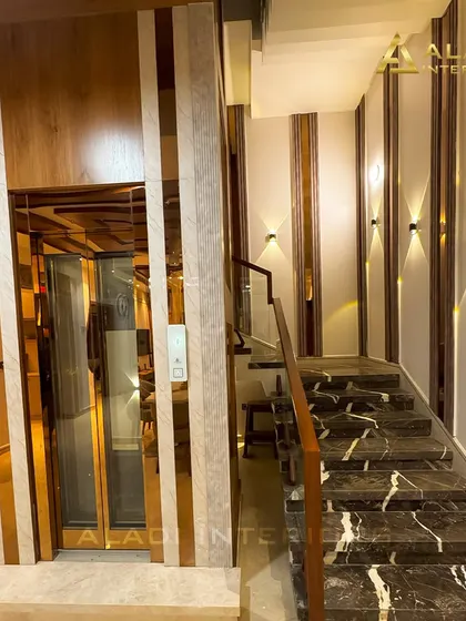 A luxurious residential elevator with glass and rose-gold finished doors, seamlessly integrated into the home's design next to a marble staircase.