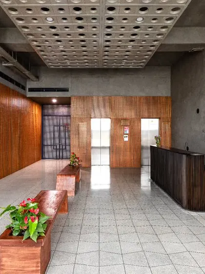 The lounge area at Anthea Pharma, featuring spacious concrete benches with a corten steel finish and a custom concrete panel ceiling. Circular lighting fixtures soften the raw industrial materials with a dynamic play of light.