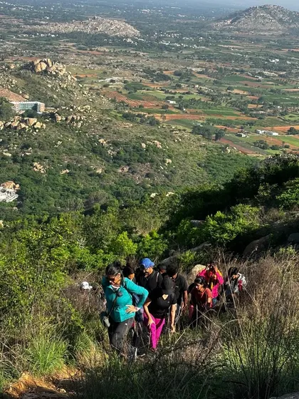 A group of trekkers hiking up a lush green hillside at Kaiwara Betta.