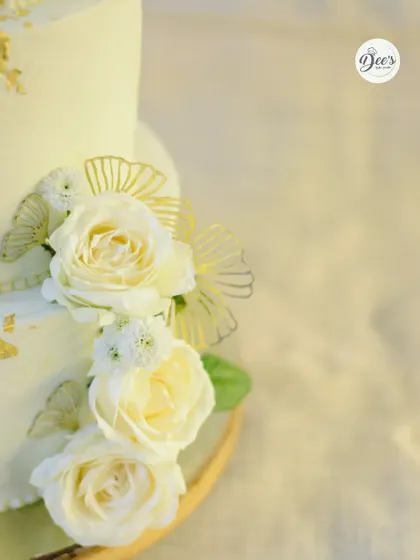 A close-up view reveals the texture of the buttercream and the delicate details of the fresh flowers and gold accents on this wedding cake.