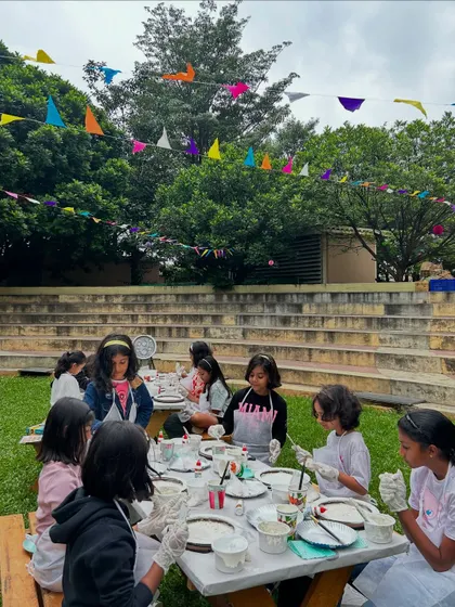 An outdoor art session in a beautiful garden setting. The kids are all focused on creating the textured surface of their moon lamps.