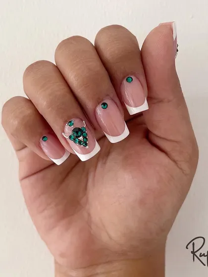 A full hand shot showing the balance of the classic French tip with the bold green crystal accent.