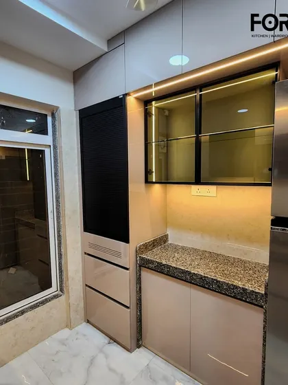 A full view of the storage and appliance wall in this kitchen. The design neatly integrates the refrigerator, a roller shutter unit, and display cabinets, ensuring a cohesive and organized look.