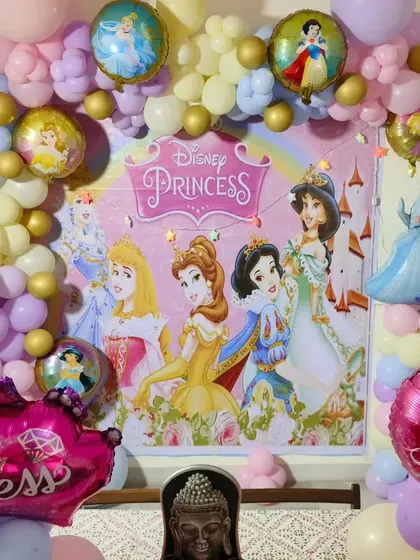 A magical Disney Princess party. This decoration uses a pastel balloon garland to frame a large backdrop featuring Cinderella, Belle, Ariel, and other princesses, creating a fairytale setting.