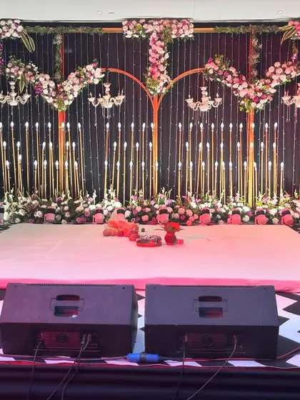 A dance floor ready for the Sangeet night. The stage is set with golden arches and floral decor, while the checkered dance floor is equipped with professional speakers for a night of performances.