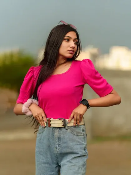 A close-up portrait focusing on the model's confident expression and the details of her pink top and belted jeans.