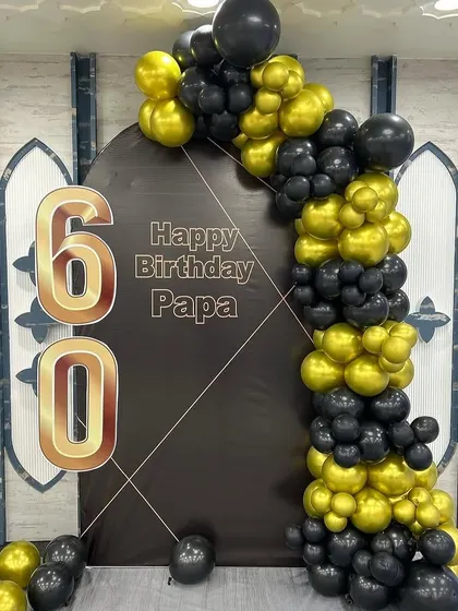 We help you celebrate the most important people in your life. This sophisticated 60th birthday decoration for a client's father uses a classic black and gold color scheme with a personalized backdrop and a bold balloon garland.