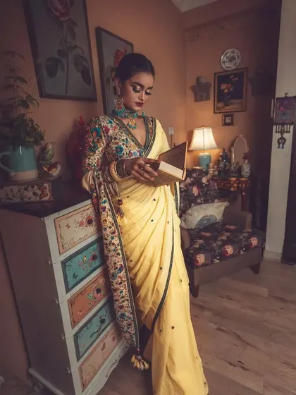 Creating a story through styling. In this shot, the model, dressed in the elegant yellow saree and embroidered blouse, interacts with the vintage-inspired set, adding a narrative quality to the fashion photograph.