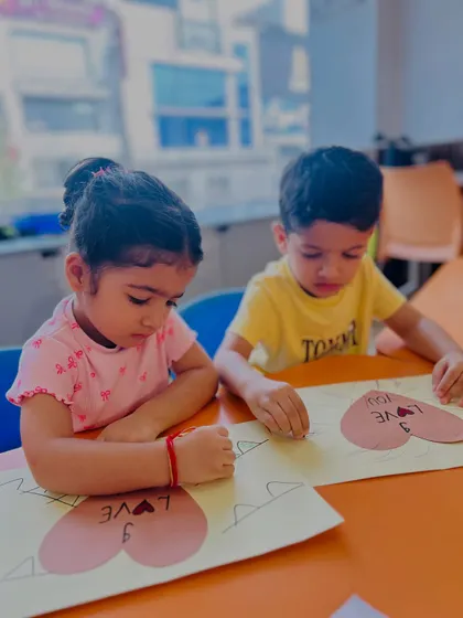 Two children work side-by-side on a "Love You" card, practicing their fine motor skills and learning to express emotions through art and words.