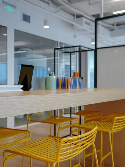 A collaborative high-top counter with bright yellow stools. These informal breakout zones are crucial in modern office design for fostering spontaneous interaction and creativity.