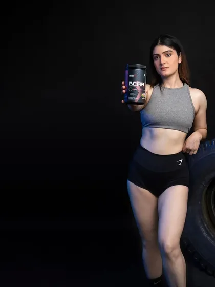 A female model leaning against a tire, holding a BCAA supplement. The use of negative space makes this image versatile for ad copy.