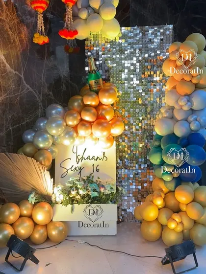 A glamorous photo corner with a silver shimmer wall, a colorful balloon arrangement, and traditional Indian floral hangings.
