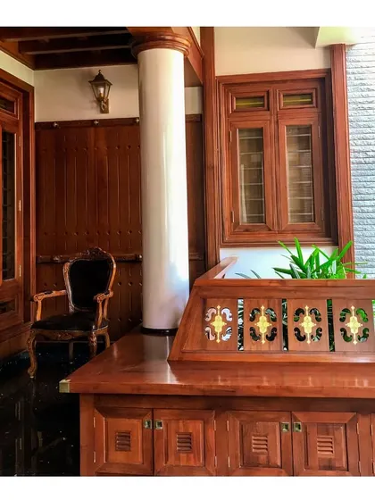 An elegant sit-out space or verandah, featuring rich wood paneling, a traditional carved bench, and a classic armchair. This area provides a tranquil transition between the interior and exterior of the home.