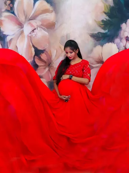 A beautiful shot of an expectant mother in a red trail gown, with the fabric spread out around her against a floral backdrop.