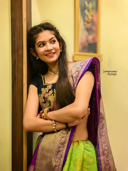 A charming portrait of a woman in a half-saree, her smile radiating warmth as she leans against a wall.