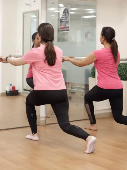 An instructor demonstrates a lunge variation at the barre, providing a clear example of the precise, controlled movements in our classes.
