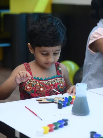 A little girl concentrates on painting her custom magnet. This activity allows for quiet focus and creativity amidst the high energy of a corporate family day.