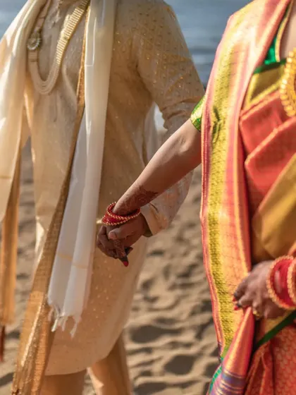 A close-up on the couple's hands, a simple gesture that signifies their union, set against the backdrop of the beach.