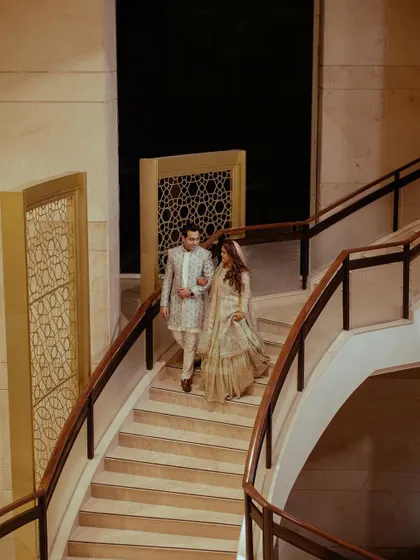 The couple makes a grand exit or entrance, walking down a beautiful marble staircase, a perfect shot from their elegant reception.