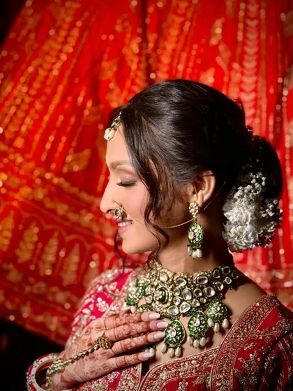 A side profile capturing the bride's serene expression, with a focus on the intricate floral bun and the stunning Polki and emerald jewelry.