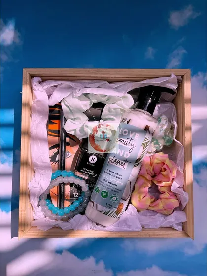 A wooden crate filled with pampering essentials. This hamper includes Love Beauty and Planet body lotion, Sugar cosmetics, and colorful scrunchies.