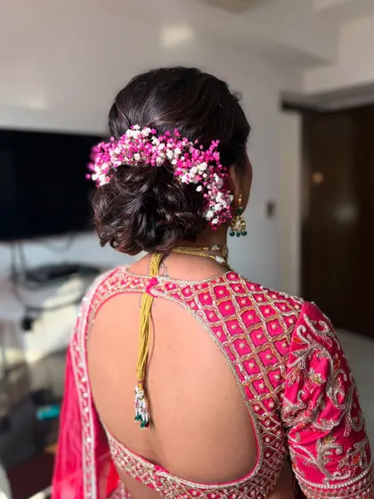 A detailed look at a textured bridal bun, intricately woven and adorned with colorful pink and white baby's breath. This style is perfect for coordinating with pastel or pink-toned outfits.