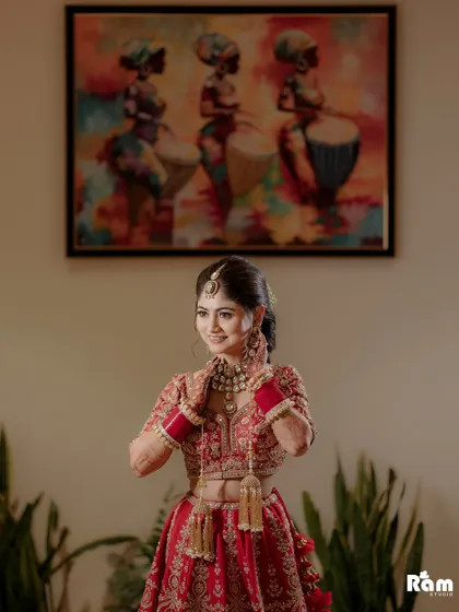 A joyful portrait of the bride in a namaste pose, her smile radiating happiness. The colorful painting in the background adds a vibrant touch to the composition.
