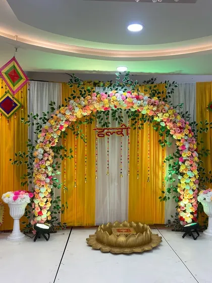 A perfect Haldi setup. This one has a beautiful floral arch in pastel colors against a bright yellow backdrop, with traditional Rajasthani umbrellas and a lotus-shaped seating area for the ceremony.