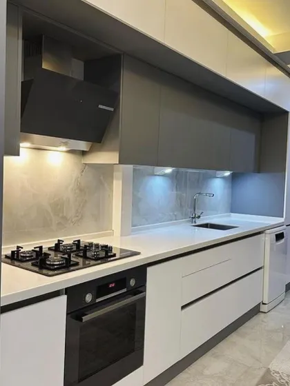 This galley kitchen in Gurgaon is designed for efficiency, with the sink, hob, and dishwasher all on one side. Under-cabinet lighting ensures the white countertop is well-lit, while the grey cabinets provide a modern contrast.