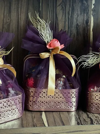 A set of three elegant Diwali hampers. The rich purple netting, gold ribbons, and delicate floral accents create a luxurious and festive look, perfect for the festival of lights.