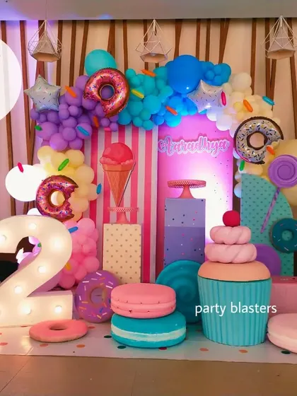 A delicious-looking Candyland theme for a second birthday. The setup is filled with giant props of donuts, macarons, cupcakes, and ice cream, creating a sweet fantasy world.